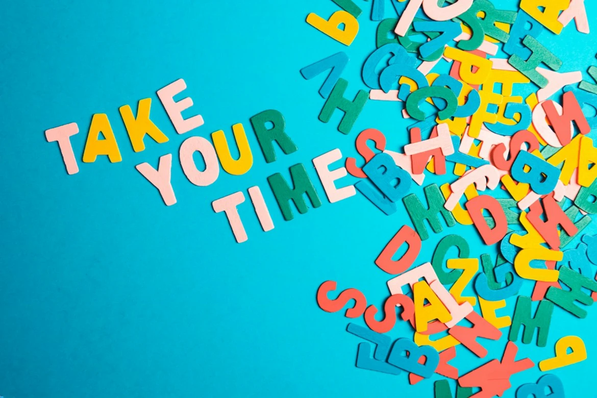 Shkronja shumëngjyrëshe prej druri që formojnë fjalët „Take your time“ mbi sfond të kaltër